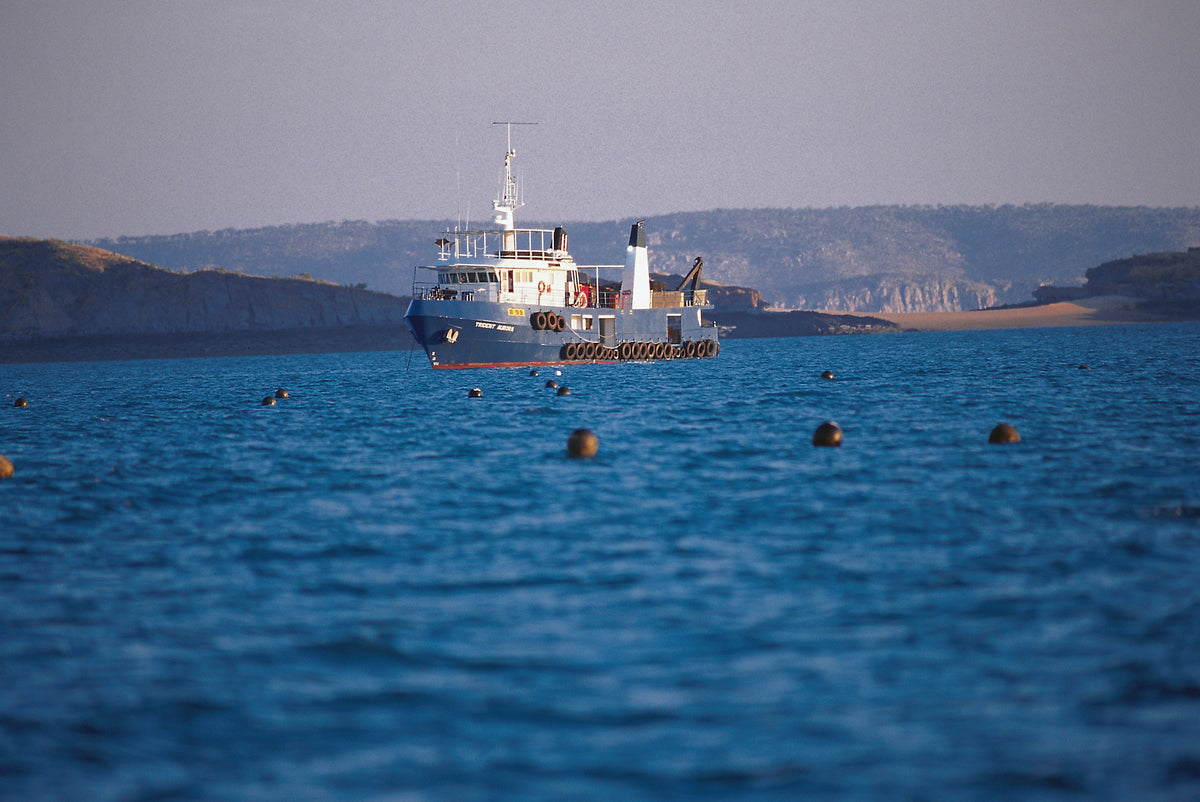 A pearling vessel at anchor beneath a low, green headland