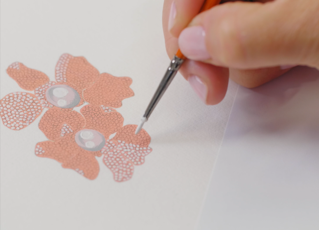 A designer hand-painting a coral-toned floral pearl jewellery design